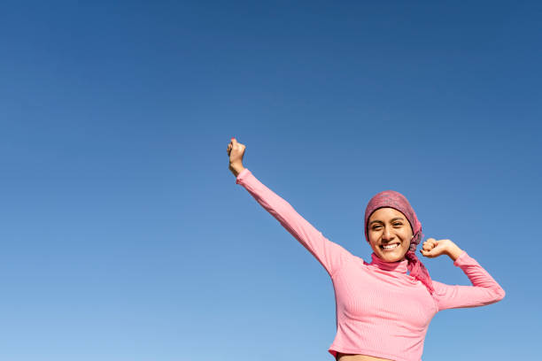 Young woman with cancer with gestures of victory and joy in the face of the disease. Celestial background and copy space. Hope, Struggle, Empowerment Concept. Young woman with breast cancer with gestures of victory and joy in the face of the disease. Celestial background and copy space. Hope, Struggle Concept. brest cancer hope stock pictures, royalty-free photos & images