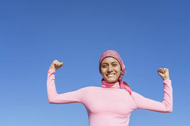 young woman with cancer showing strength with her smile and arms raised, light blue background and copy space. hope, struggle, empowerment concept. - spring happiness women latin american and hispanic ethnicity imagens e fotografias de stock