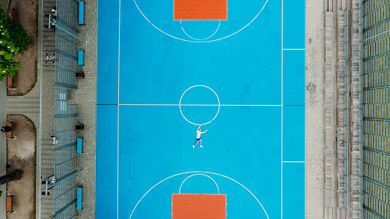 Scenic drone aerial photo of a man lying down holding the basketball circle at the colorful playground outdoors