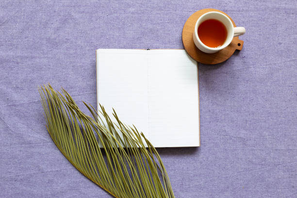 Empty notebook with green leaf, cup of tea on purple fabric background. flat lay, top view, copy space