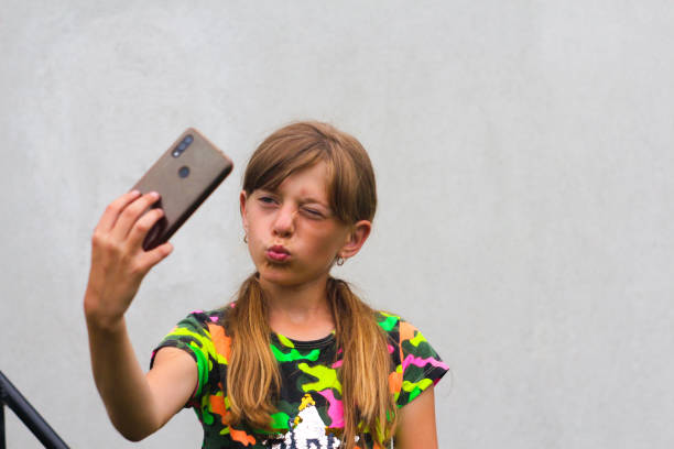 Defocus self-portrait. Preteen girl poses and takes a selfie. Cheerfull little girl taking a photo with a smart phone. Gray white background. Smiling attractive girl is having fun. Out of focus Defocus self-portrait. Preteen girl poses and takes a selfie. Cheerfull little girl taking a photo with a smart phone. Gray white background. Smiling attractive girl is having fun. Out of focus. child 10 11 years 8 9 years cheerful stock pictures, royalty-free photos & images