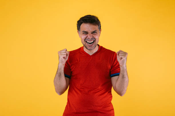 Soccer fan in red jersey clenches arms excitedly and screams stock photo