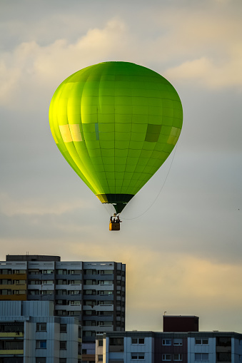 Green hot air balloon flying over city buildings