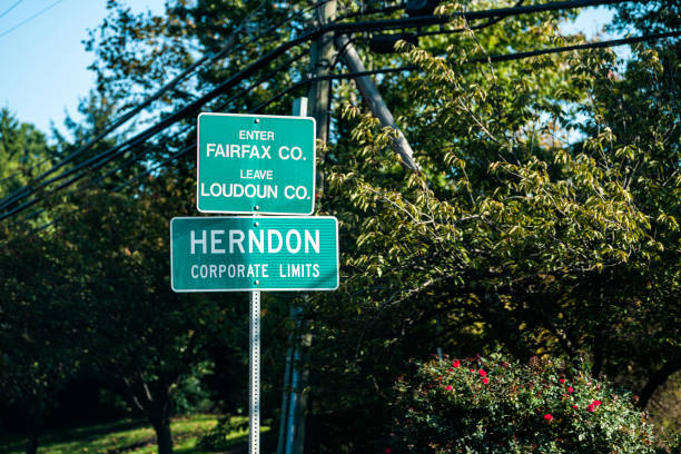 Road sign for city or town of Herndon corporate limits with enter Fairfax leave Loudoun county in Northern Virginia suburbs by green trees park near Washington DC Road sign for city or town of Herndon corporate limits with enter Fairfax leave Loudoun county in Northern Virginia suburbs by green trees park near Washington DC fairfax virginia photos stock pictures, royalty-free photos & images