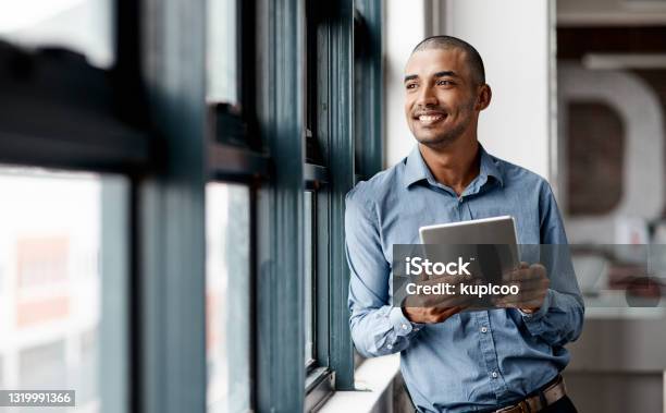 Shot Of A Young Businessman Using A Digital Tablet While Standing At A Window In An Office Stock Photo - Download Image Now
