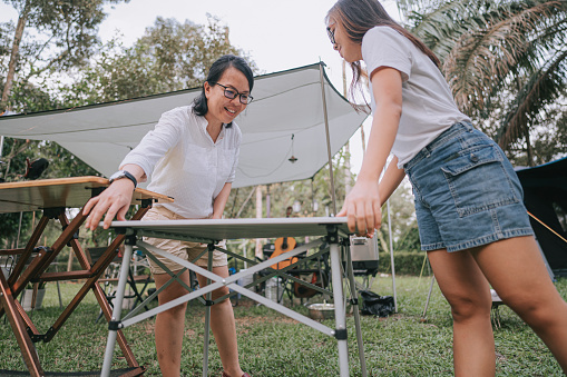 low angle view asian chinese mother and daughter setting up picnic table for food preparation at camping site