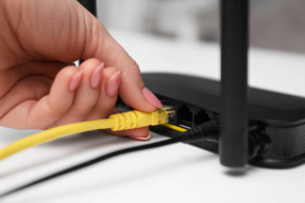 istock Woman connecting cable to router at white table, closeup. Wireless internet communication 1319995920