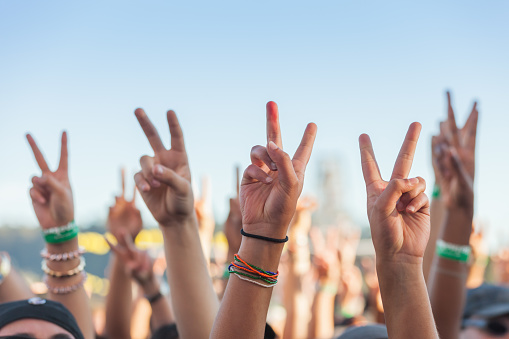 A series of hands raised in the air above people's heads giving the peace sign at a rally, protest, concert outside on a sunny day