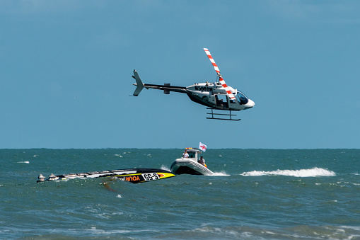 Cocoa Beach, Florida, USA - May 23, 2021: The race boat Yourstorageunit capsized just after getting airborne at the Thunder on The Beach power boat race catamaran division.  A rescue helicopter and a powerboat seek to assist. THere is an emergency flare on the water. This is part of a series depicting the capsizing of this boat.