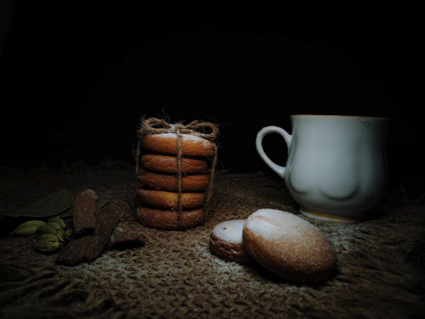 istock Composition of hot Brewed Tea Or Coffee and Homebaked Wheat Cookies Or Biscuits flavoured with Cinnamon roll, Cardamom, Bayleaf isolated in a Dark Rustic Background. 1320002086