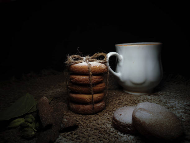 istock Composition of hot Brewed Tea Or Coffee and Homebaked Wheat Cookies Or Biscuits flavoured with Cinnamon roll, Cardamom, Bayleaf isolated in a Dark Rustic Background. 1320002087