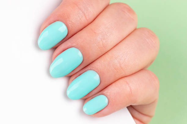 istock Female hand with beautiful manicure - mint blue nails with white smartphone on green background, closeup. Selective focus 1320004746