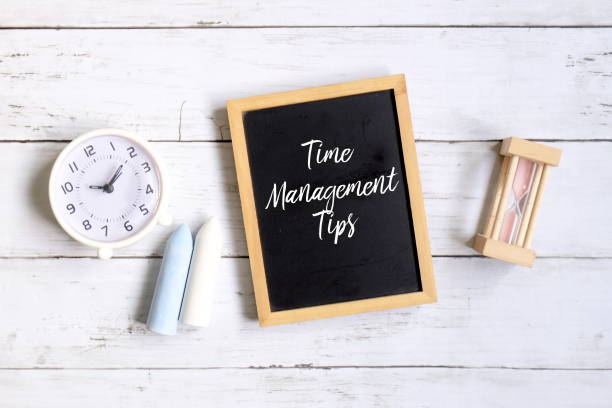istock Top view of chalk,table clock,hourglass and blackboard written with 'TIME MANAGEMENT TIPS' on white wooden background. 1320004805