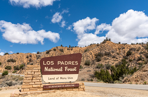 Los Padres National Forest, CA, USA - May 21, 2021: Beige on brown sign at entrance of the park under blue cloudscape. mountain range in back.