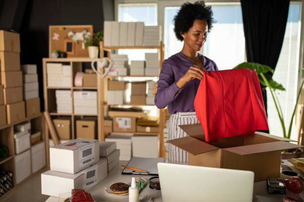 istock Female entrepreneur folding a shirt and packing it in a box 1320007058