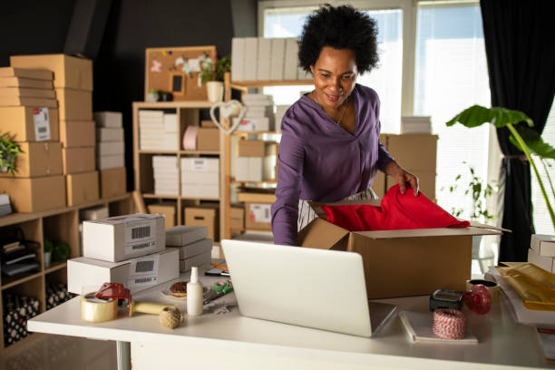 istock Businesswoman using laptop while packing clothes in a cardboard box 1320007085