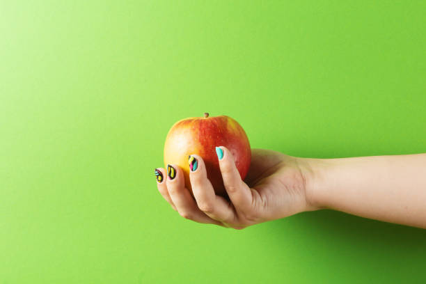 istock Female hand with colorful manicure holding apple on green background 1320007274