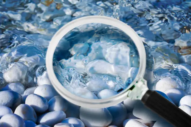 Control of purity and quality of water in nature - concept image with water of a stream seen through a magnifying glass.