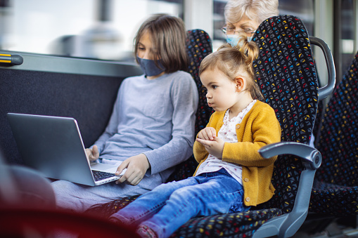Boy and little girl looking at laptop while their grandmother sitting behind them. Other people are in the bus too.