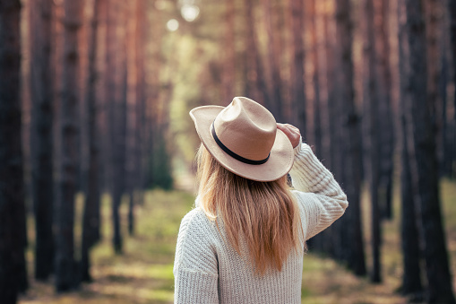 Boho woman wearing hat and knitted sweater in woodland. Woman is enjoying fresh air outdoors in nature