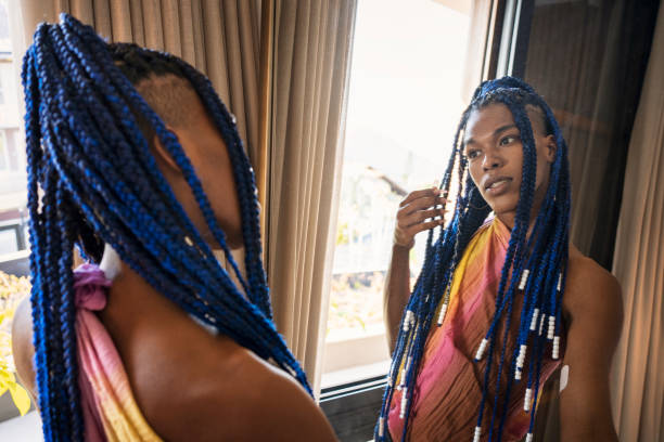 Transgender afro woman taking care of her braids in the mirror Beautiful transgender woman looking in the mirror and taking care of her braids at home. combing photos stock pictures, royalty-free photos & images