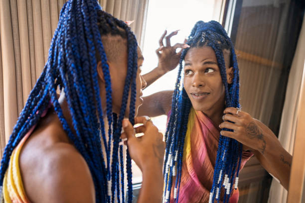 Transgender afro woman taking care of her braids in the mirror Beautiful transgender woman looking in the mirror and taking care of her braids at home. black woman hair braids stock pictures, royalty-free photos & images