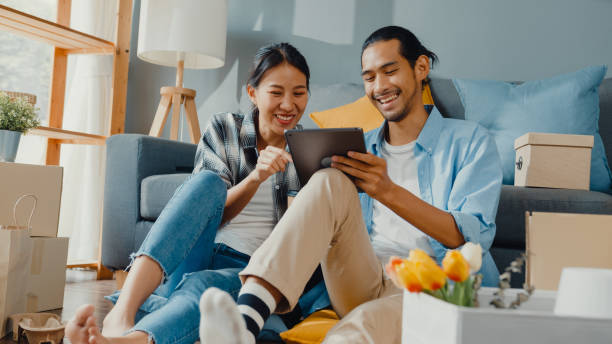 casal jovem e atraente asiático feliz homem e mulher usam tablet online despaia casa de decoração com pacote de caixa se movem em casa nova. - the new ipad - fotografias e filmes do acervo