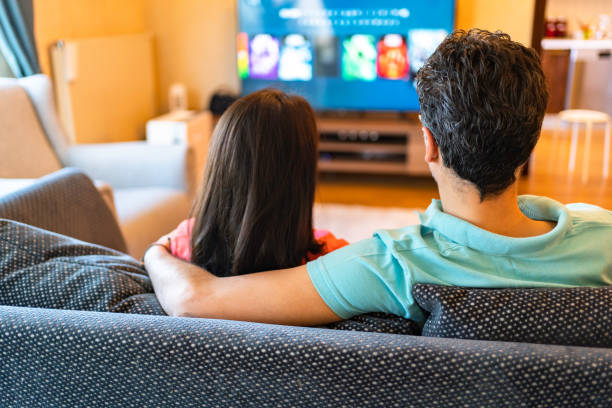 istock Couple Watching TV Relaxing Sitting On Sofa At Home 1320020641