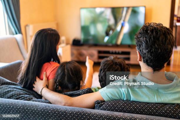 Parents And Their Two Children Watching Tv Together At Home Stock Photo - Download Image Now