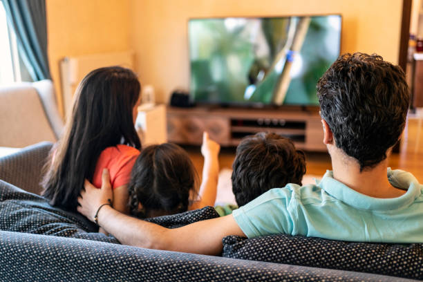 parents and their two children watching tv together at home - arts and entertainment imagens e fotografias de stock