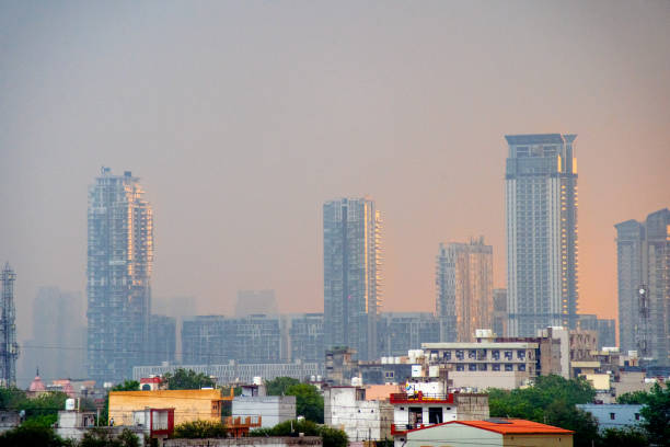 zoomé dans le projectile affichant des gratte-ciel en verre multi étages plancher de grands bâtiments sur une aube pluvieuse allumée du côté par le soleil orange affichant la croissance rapide de la propriété d’immobiliers dans gurgaon delhi mumb - bangalore india business building exterior photos et images de collection