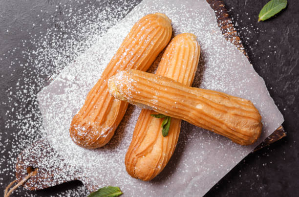 3 eclairs with powdered sugar on a dark background, top view, dissert, 3 eclairs with powdered sugar on a dark background, top view, dissert, dissert stock pictures, royalty-free photos & images