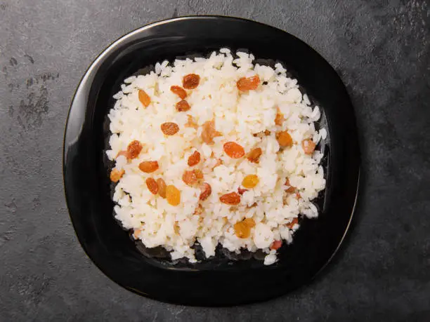 caucasian sweet pilaf with raisins on a black plate top view, rice with dried fruits