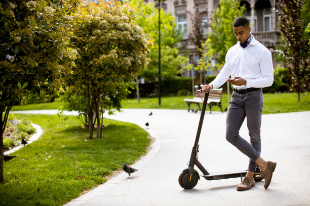 istock Young African American using mobile phone while standing by electric scooter on a street 1320034816