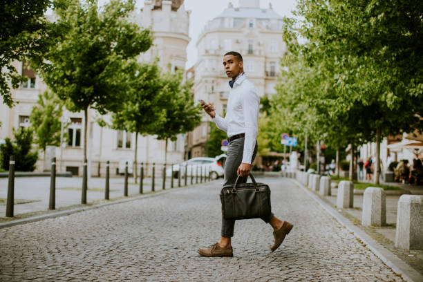 istock Young African American businessman using a mobile phone while crossing a street 1320034824