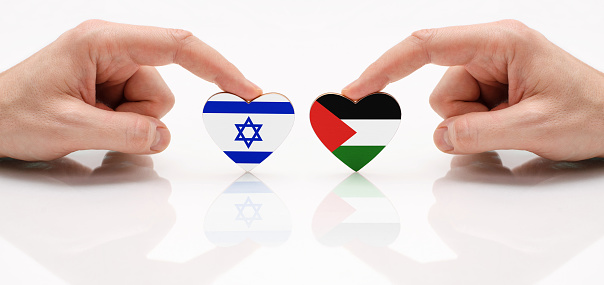 The concept of friendship and diplomatic relations between Israel and Palestine. Two male hands are holding flags in the shape of a heart on a glass table. The flag of Israel and Palestine as a symbol of truce