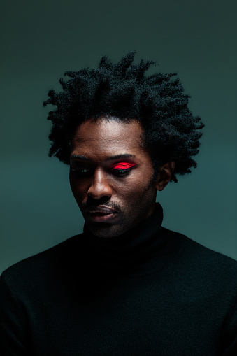 Afro american man wearing black turtleneck and red make-up on eye. Headshot on green background.