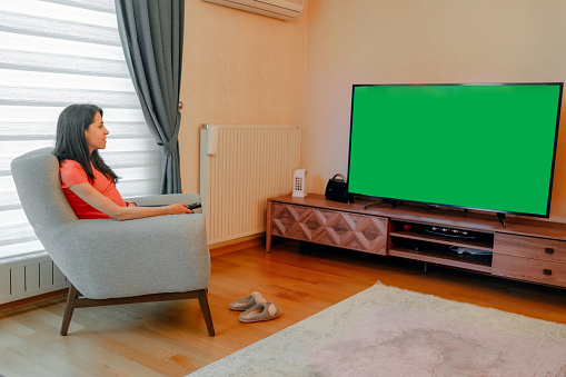 women Sitting At Home in the Living Room on His Chair, Watching Green Chroma Key Screen