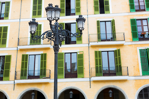 Beautiful street lamp. Yellow house wall with green shutters on the windows in the Mediterranean style