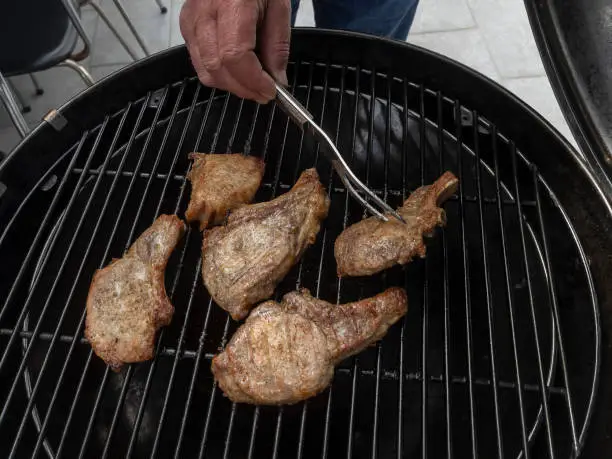 Human hand with a fork turns tasty and delicious roasted pork chops on a gas grill