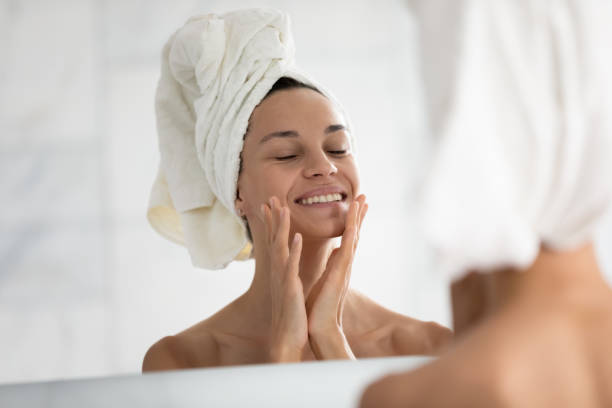 istock Happy woman with towel on head touching face at mirror 1320048344