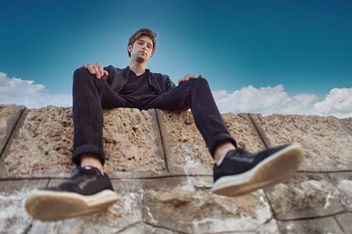 Concept of arrogance and  importance, young white male looking from above while sitting on stone wall.