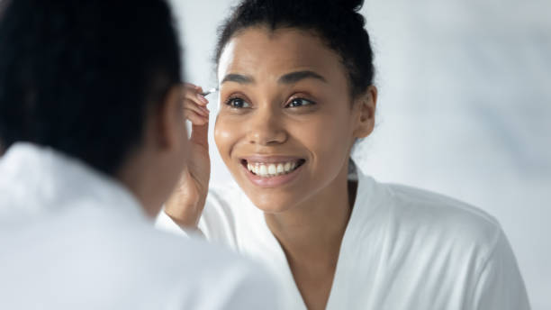 istock Happy engaged Black millennial girl in bathrobe plucking eyebrows 1320049936