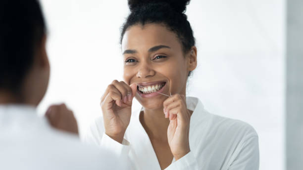 istock Happy Black girl in bathrobe cleaning white teeth with floss 1320049945
