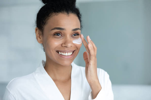 istock Smiling Afro American woman in bathrobe spreading moisturizing collagen cream 1320049980