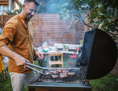 Photo of a young man grilling meat on the barbecue party in backyard