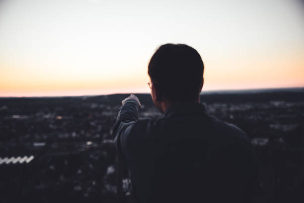 istock Teenage Man Pointing into the Sunset Outdoors on Hill Top 1320054713