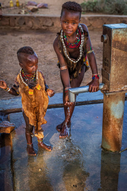 african little girl drinking water from hand water pump, ethiopia, africa - hamer woman imagens e fotografias de stock