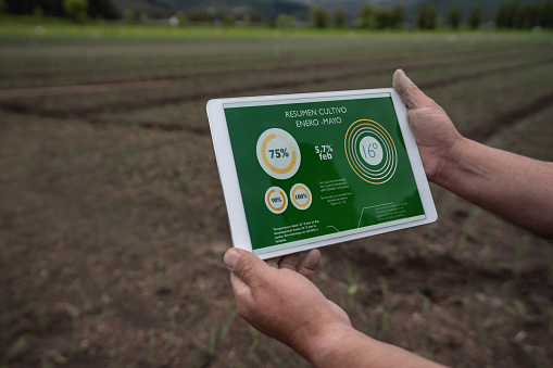 Close-up on a farmer using an app on a tablet computer to track the productivity of his soil for harvesting - agriculture concepts. **DESIGN ON SCREEN WAS MADE FROM SCRATCH BY US**