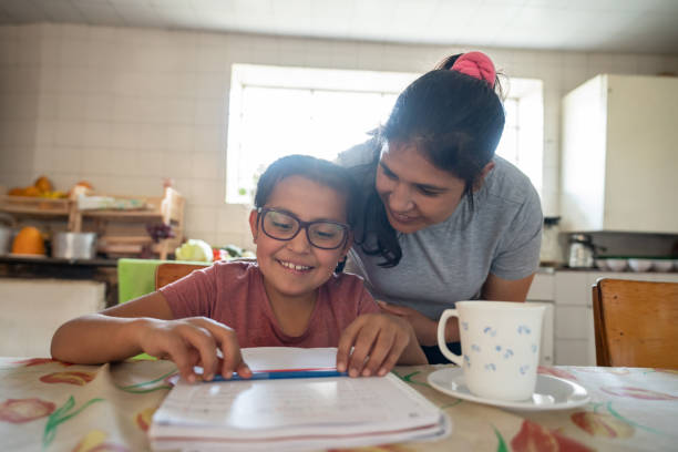 Happy girl doing her homework with the supervision of her mother Happy Latin American girl doing her homework with the supervision of her mother - education concepts poverty photos stock pictures, royalty-free photos & images